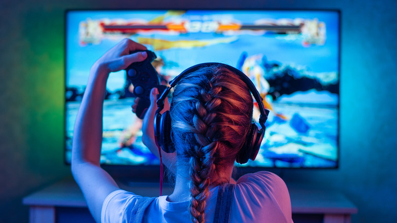 Young girl wearing headphones sitting in front of a TV playing video games