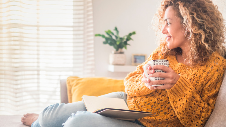 a woman on her couch with a coffee cup and book 