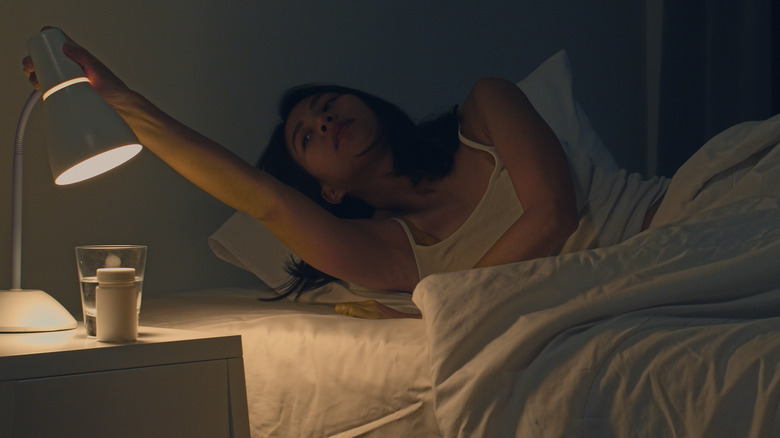 woman adjusting lamp from bed