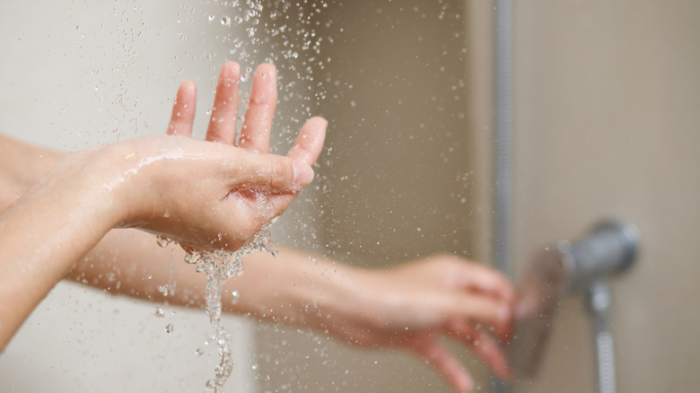 A person's hand in the shower with water droplets coming down