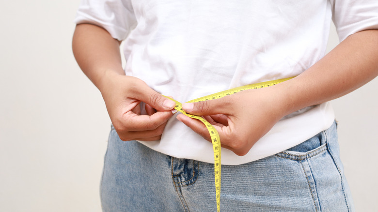 A woman measuring her waist with a measuring tape