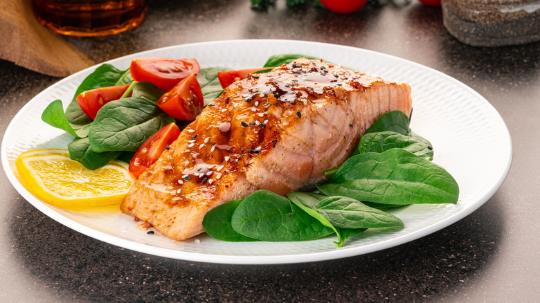 Fish on plate alongside greens, tomatoes, and citrus