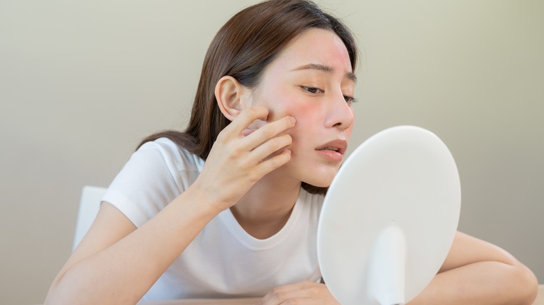 woman examines skin in mirror