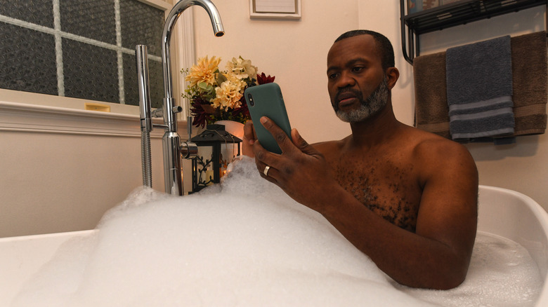 Man in bath tub looking at smart phone