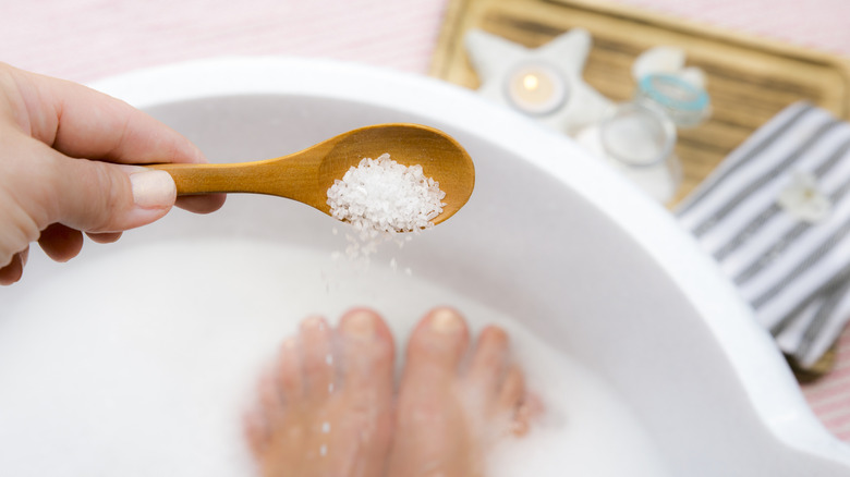 A woman's hand adding a spoonful of Epsom salts to her bath