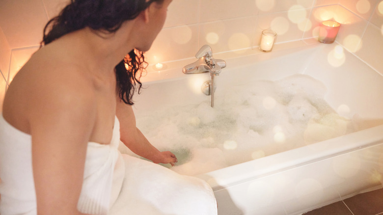 A woman using her hand to test the temperature of her bath water