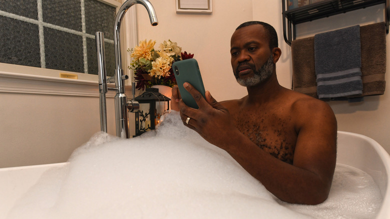 Man in bath tub looking at smart phone