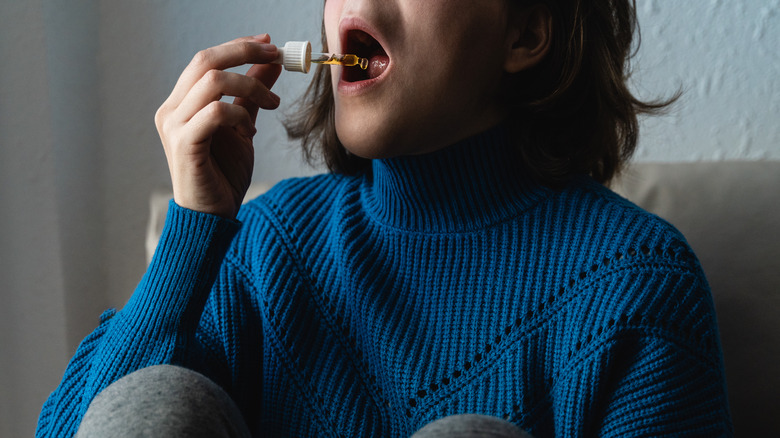 Woman in blue sweater using CBD oil dropper under her tongue