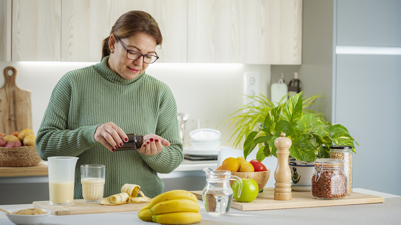 woman standing in her kitchen and taking her supplements