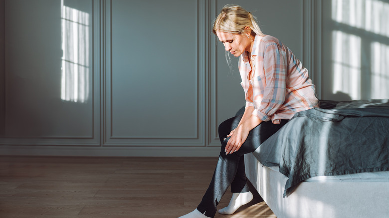 Woman sitting on bed and rubbing injured leg