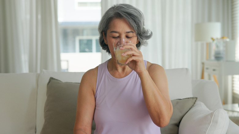 A mature woman sitting on a sofa drinking a beverage