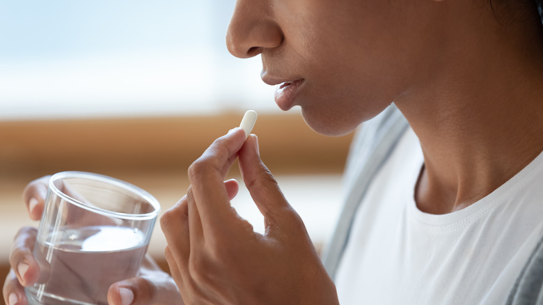 person holding pill and glass of water