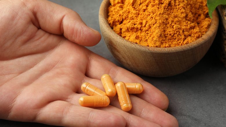A hand holding turmeric supplement pills next to turmeric powder