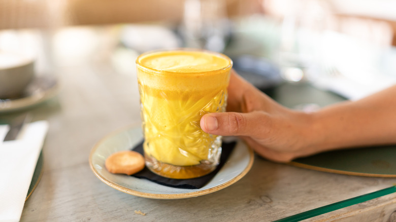 A hand grabbing a glass of golden milk