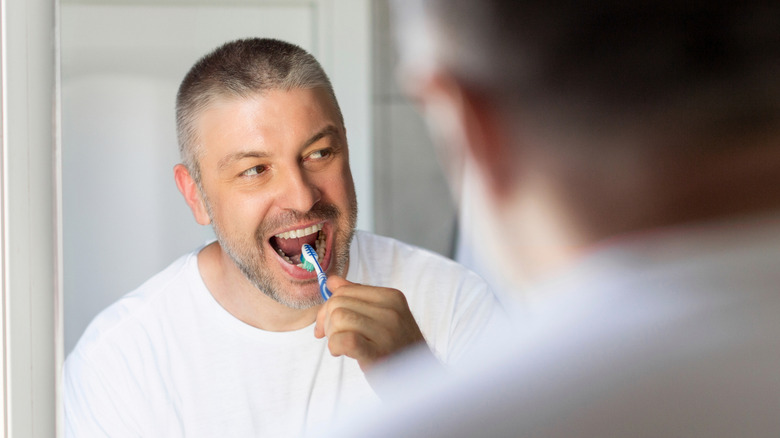An over 50 man brushing his teeth in front of the mirror