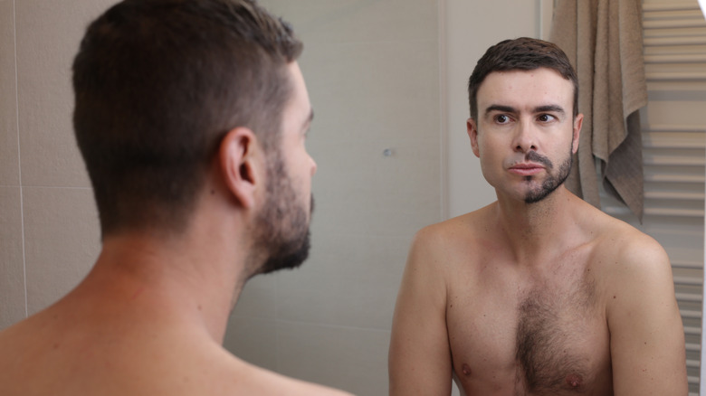 Male with half shaven beard and chest peering into a mirror