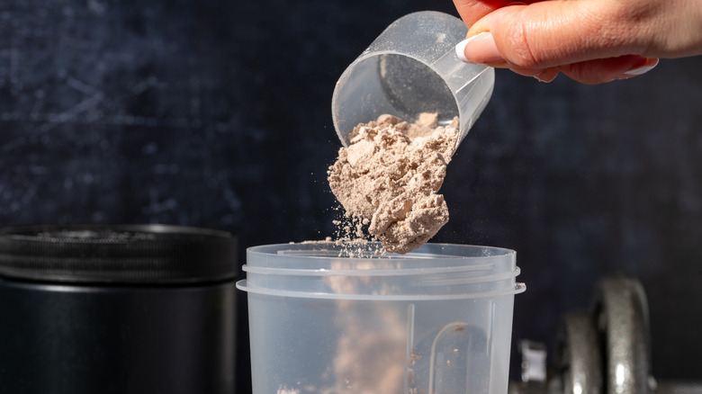 A scoop of chocolate protein powder dropping into a shaker bottle