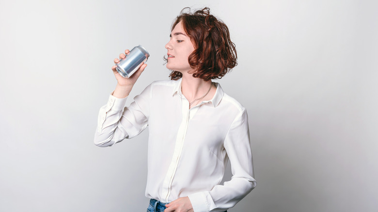 A woman drinks a canned drink