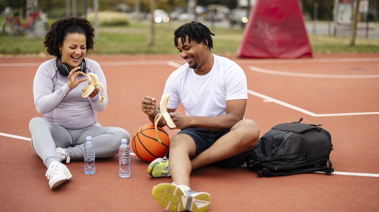 young couple eating bananas on basketball court