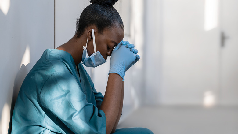 An exhausted nurse leans against the wall