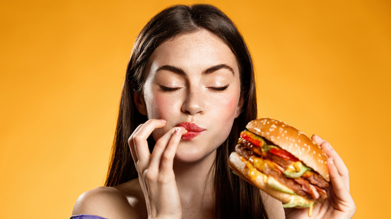 young woman closes her eyes and licks her lips while she holds giant, juicy burger