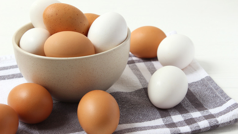 Bowl of white and brown eggs with some on table