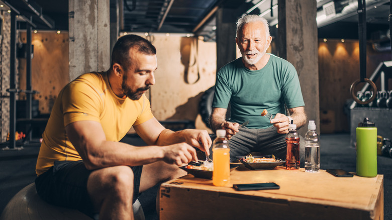 Two men eating high-protein meals at gym