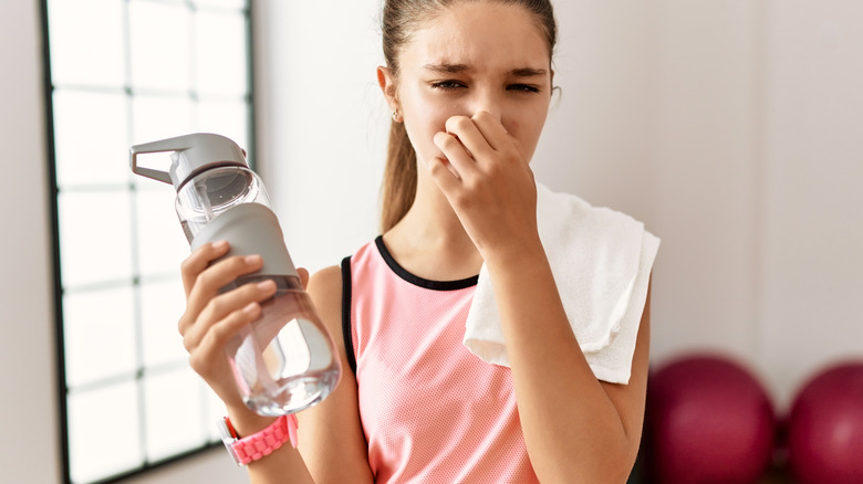 Woman holding water tumbler pinching nose