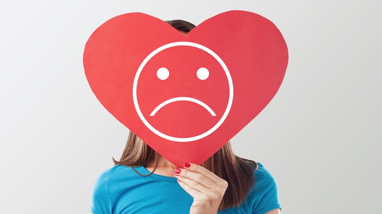 teenager holding a sad heart over her face