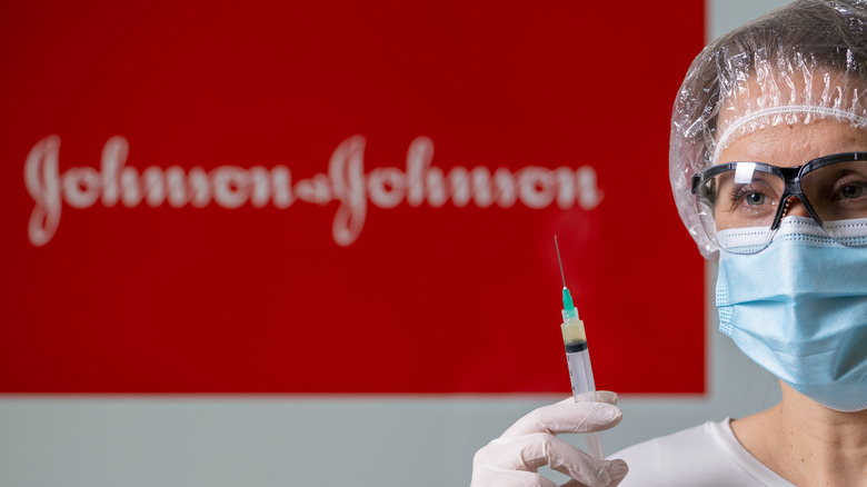 Masked doctor with syringe standing in front of a red Johnson & Johnson sign