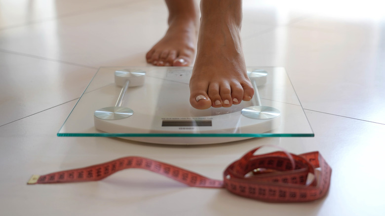 female feet stepping on a scale with a tape measure in foreground
