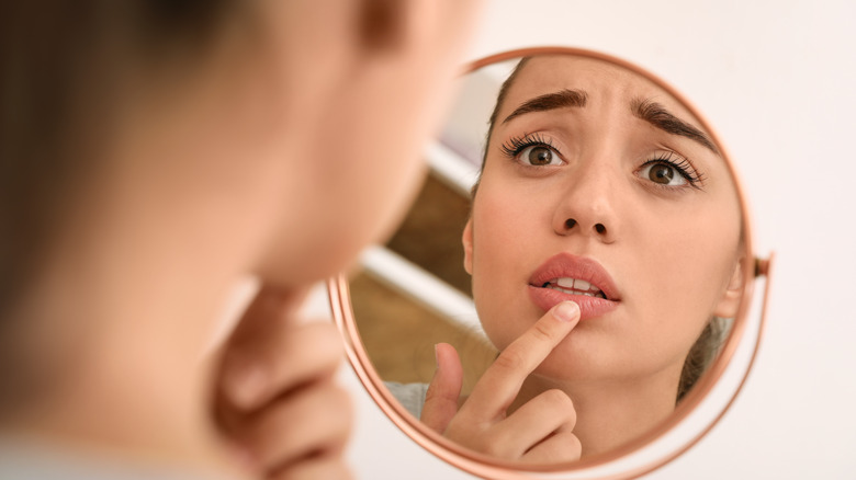 woman looking in mirror with chapped lips