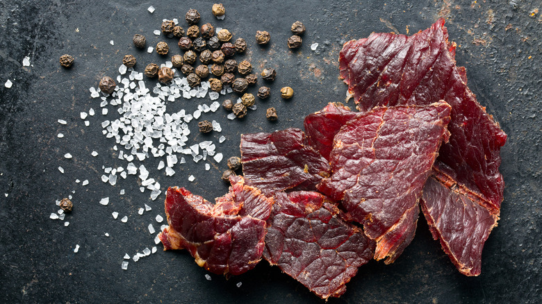 Beef jerky next to salt and peppercorns 