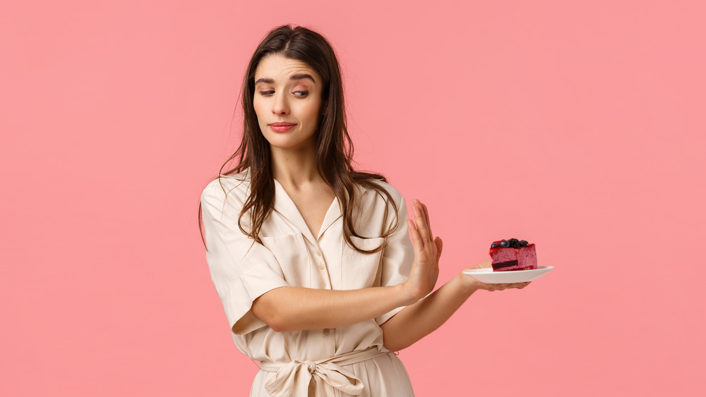 A woman refusing cake with all pink background 