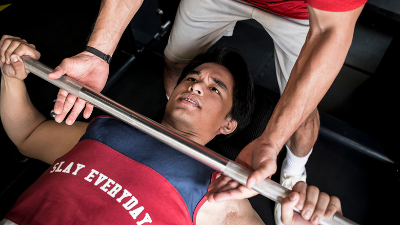 Man bench pressing with assistance