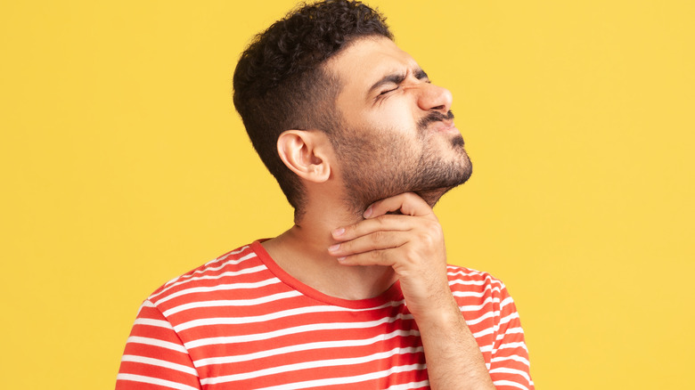 Squinting man touching throat