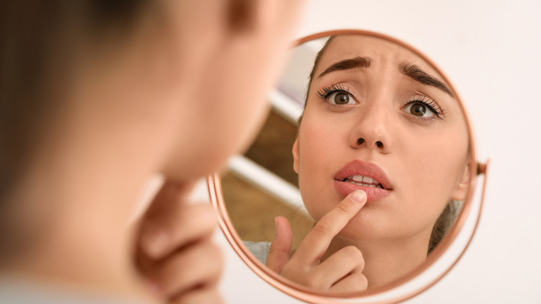 woman looking in mirror with chapped lips