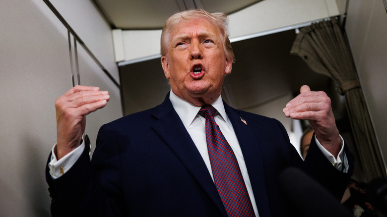 President Donald Trump from below, he gestures with both hands, mouth squeezed into an o as he talks on Air Force One.
