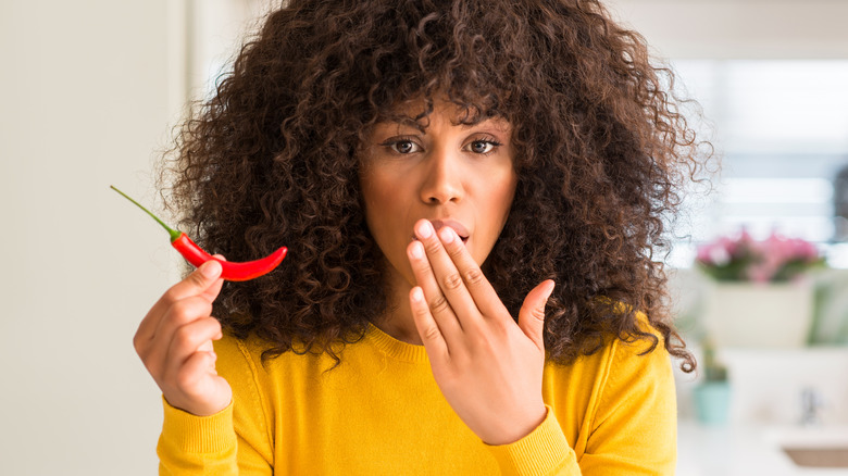 woman covering her mouth while holding a hot pepper