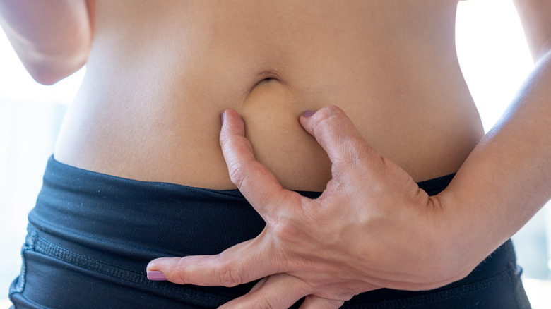 Close up of hand and two painted fingernails touching around their belly button