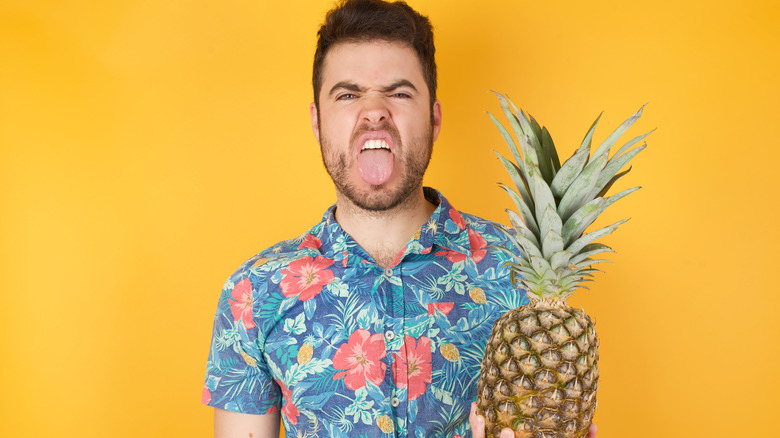 Man holding pineapple sticking out tongue