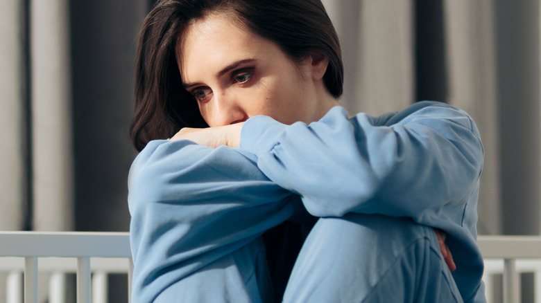 Woman sits sadly beside an empty crib