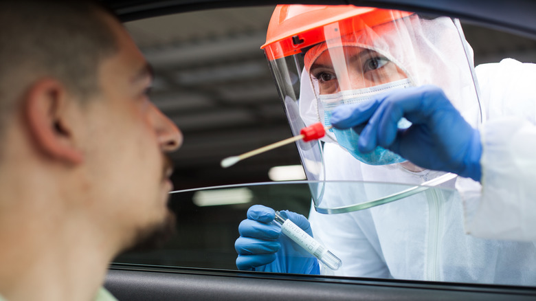 Man receiving a swab COVID-19 test from a masked woman in hazmat suit