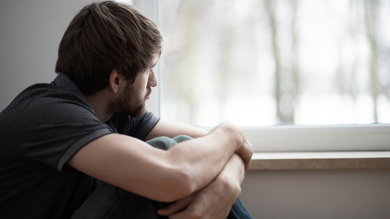 Young man looking sad out a window