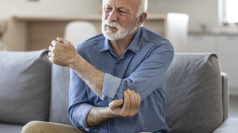 Pained elderly man rubbing left arm