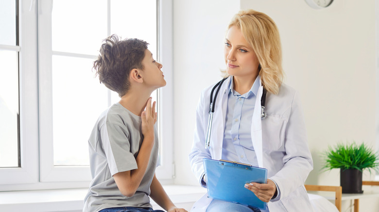 A boy holding his throat while sitting with a doctor