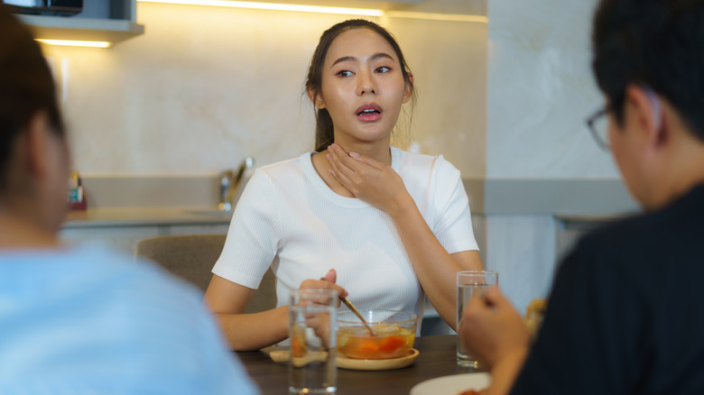 A woman holding her throat while eating a fruit salad