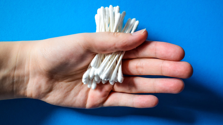 A hand holding cotton swabs on a blue background