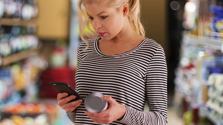 A woman looking at a tuna can label and her phone