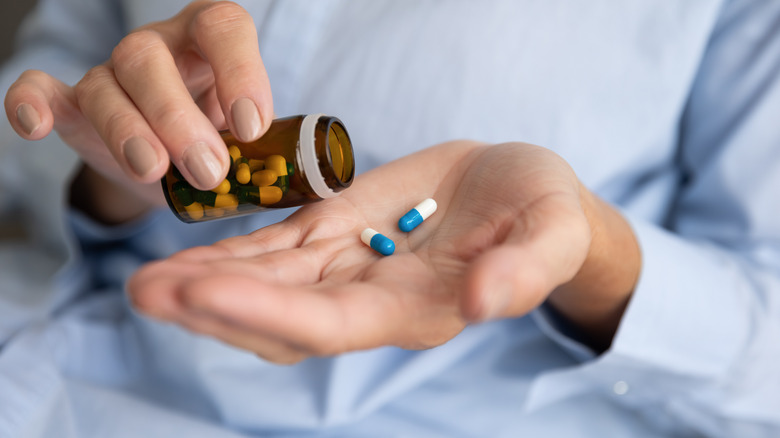 person holding pill bottle and pills